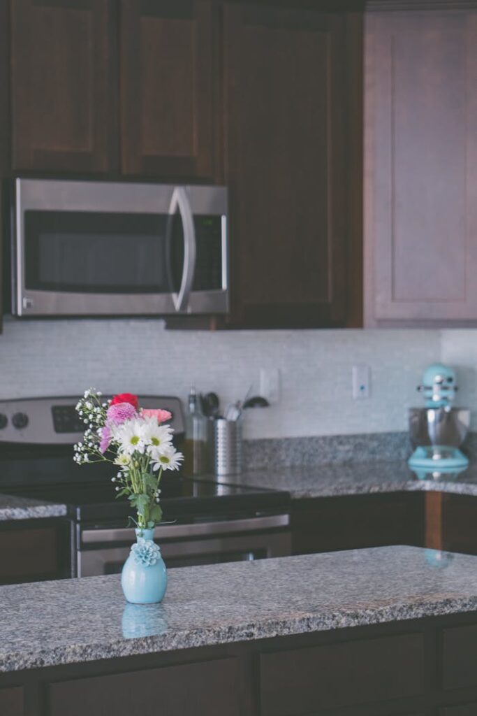 pexels-photo-1103560 Stylish kitchen interior featuring granite countertops, dark wood cabinets, and a floral vase centerpiece.
