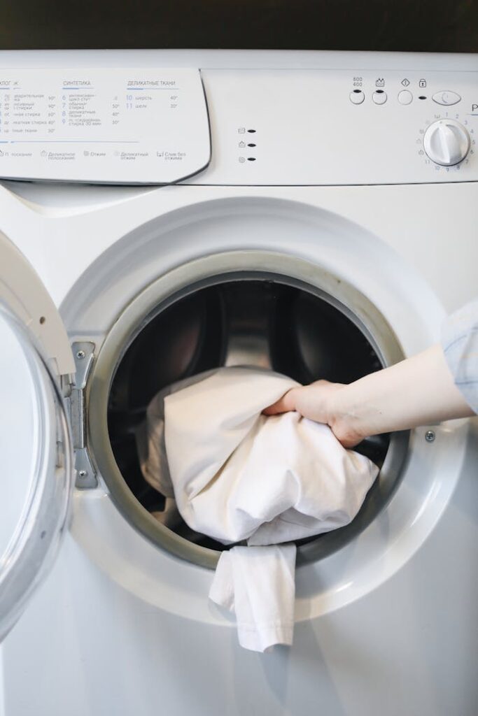 pexels-photo-4440652 Close-up of a person's hand putting laundry into a front-loading washing machine.